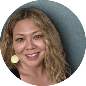 An Asian lady with long blonde hair smiles to the camera. She has gold circular earrings on and soft brown eyes.