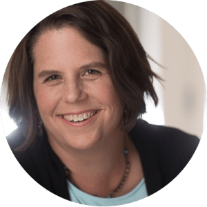 A close up of a lady with short dark hair. She is smiling and wearing a thin beaded necklace.