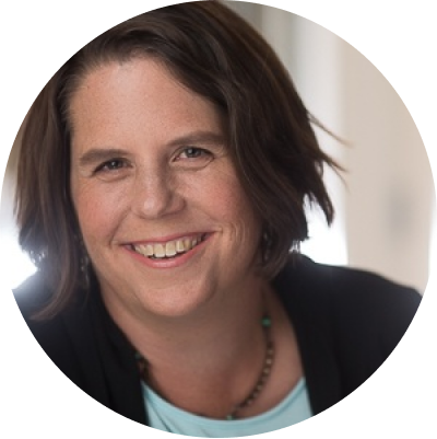A close up of a lady with short dark hair. She is smiling and wearing a thin beaded necklace.